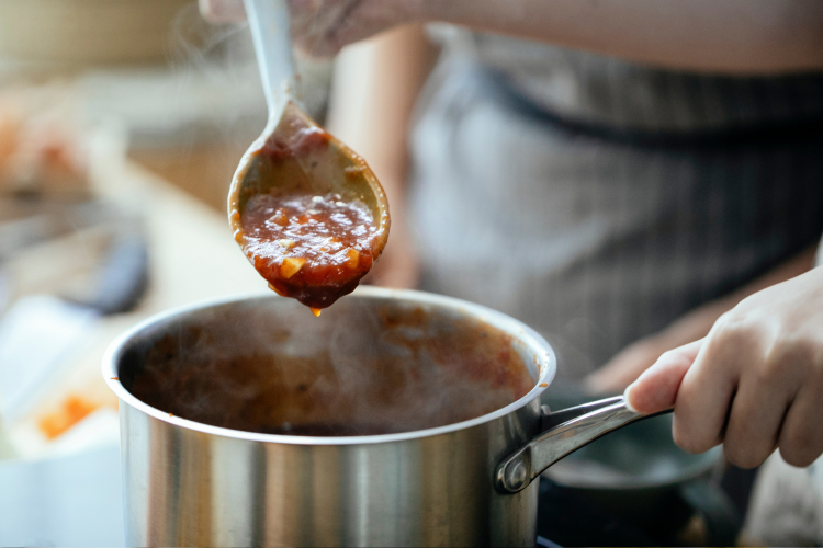 woman stirring sauce in a stainless steel pot