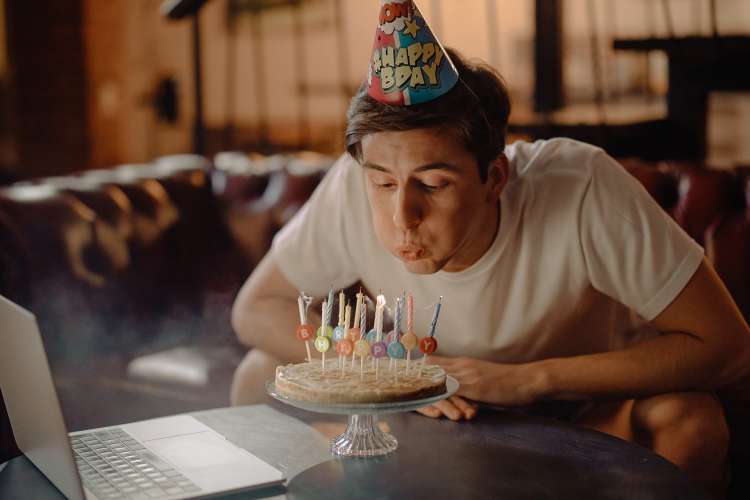 young man blowing out candles during a virtual birthday party