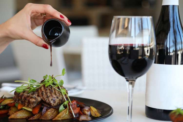 pouring demi glass over filet with an accompanying glass of pinot noir