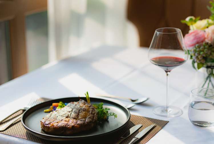 steak with vegetables plated on a table alongside a glass of red wine