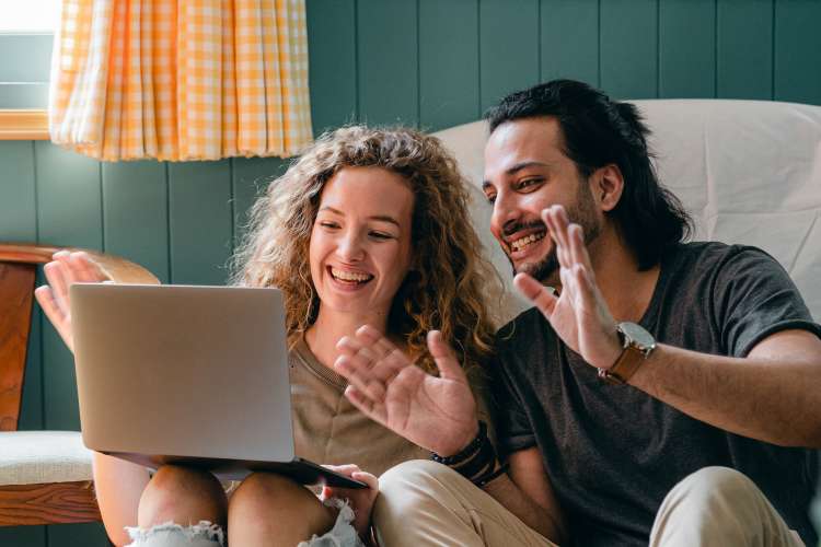 young couple waving to laptop screen during video call