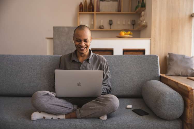 man sitting on the couch with laptop playing online team building games