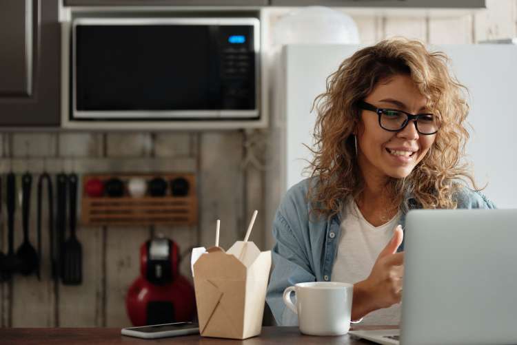 woman with takeout using laptop to play virtual games with remote teammates