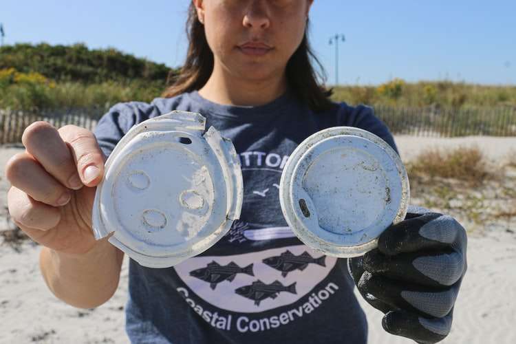 Hands hold up trash collected from the beach during community service-based team building activities