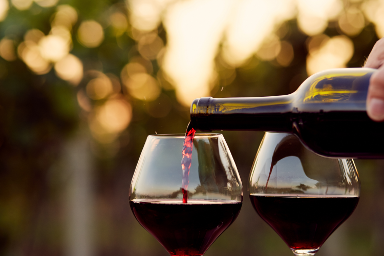 pouring red wine into a pair of wine glasses