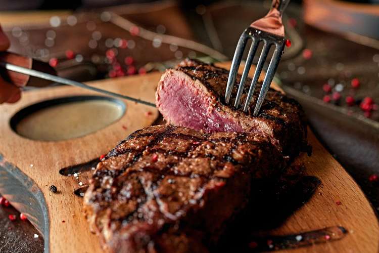 slicing ribeye steak on a cutting board