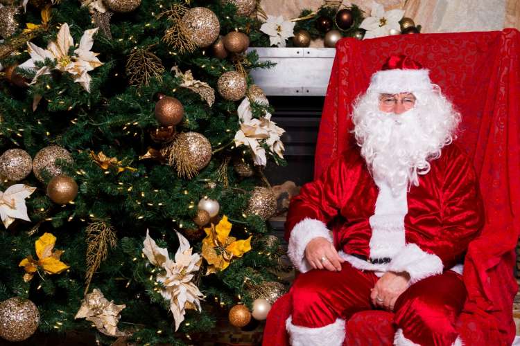 santa claus sitting next to a christmas tree