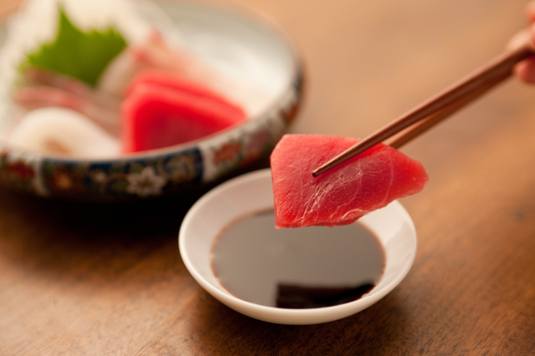 chopsticks dipping sashimi in soy sauce