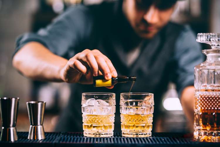 A man pouring liquid into two glasses during a mixology class, which is a great 50th birthday party idea