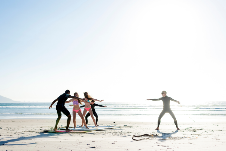 friends on a beach taking surfing lessons with an instructor