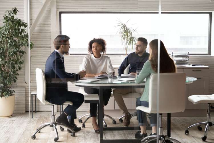 four professionals sit around a table in a glass room talking