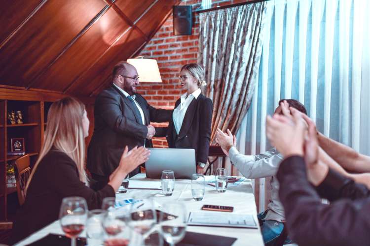 a professional is congratulated by her boss as co-workers applaud