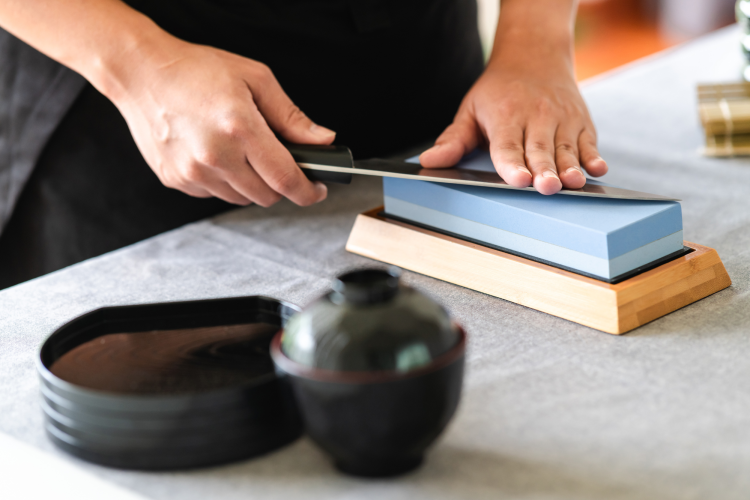 chef using a whetstone to sharpen a knife