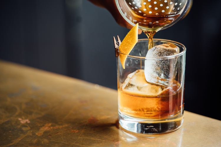 pouring a whiskey over ice with orange peel