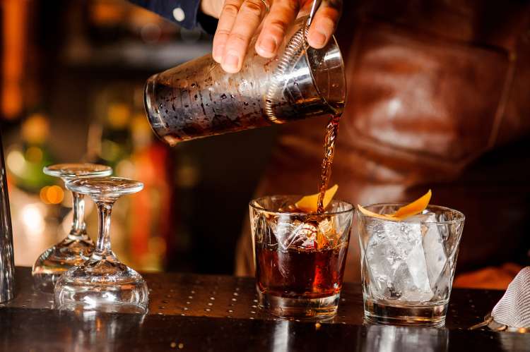 mixologist pouring a whiskey cocktail