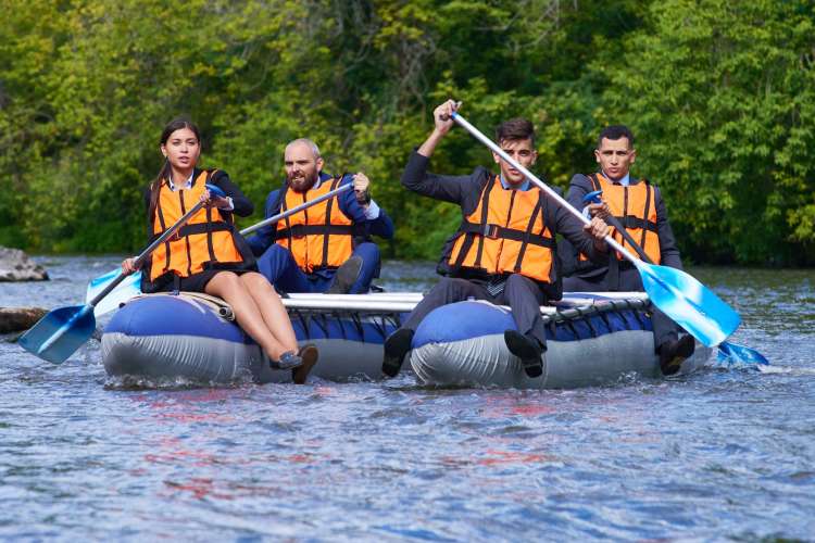 four people in orange vests paddling in rafts