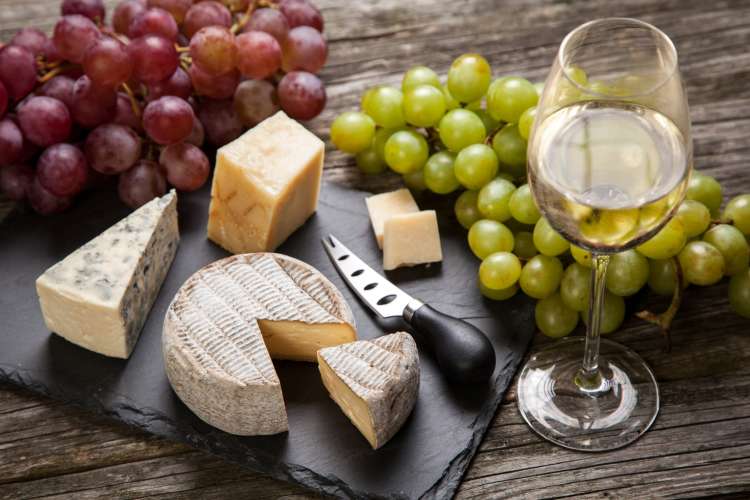 cheese on a slate board with grapes and white wine