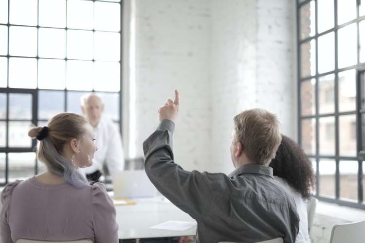 Four people having a work discussion, one of them with a raised hand