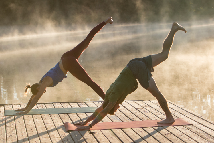 couple doing yoga outdoors on a dock