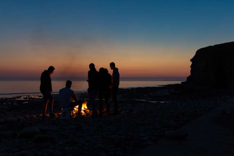 friends gathered around a beach bonfire at sunset