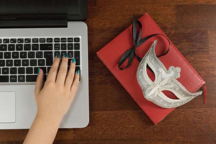 hand on laptop next to masquerade mask