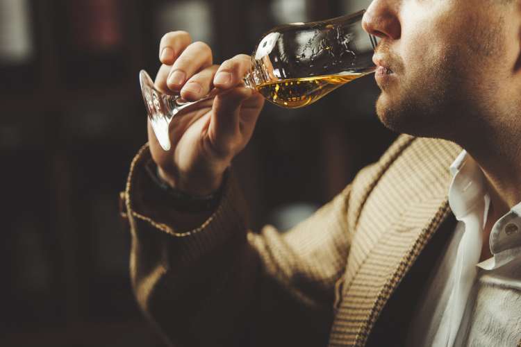 person taking sip of whiskey from glass