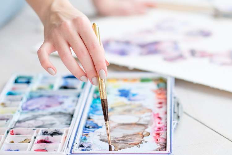 hand with paintbrush mixing watercolor paints