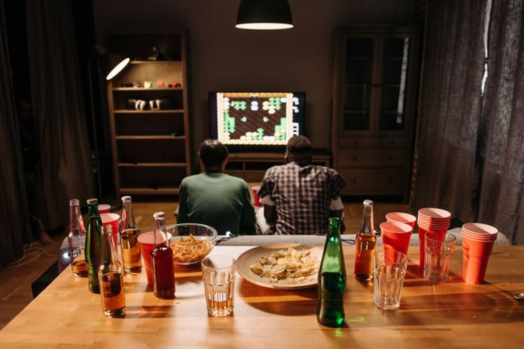 two men sit gaming surrounded by drinks and snacks