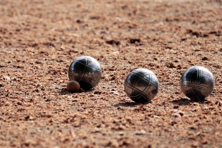 three bocce balls sit on a sandy surface close to a small target ball