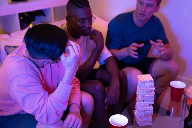 three men sit playing drunk jenga with cups and snacks around them