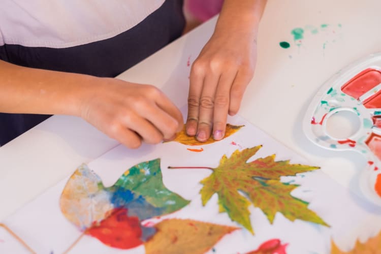 A kid crafting with paint and leaves.