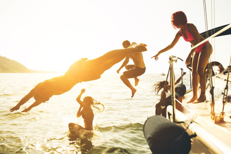 People diving off a boat at sunset.