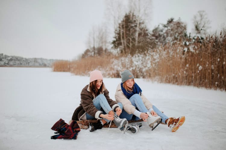 Two girls tying up their ice skates at an outdoor rink.