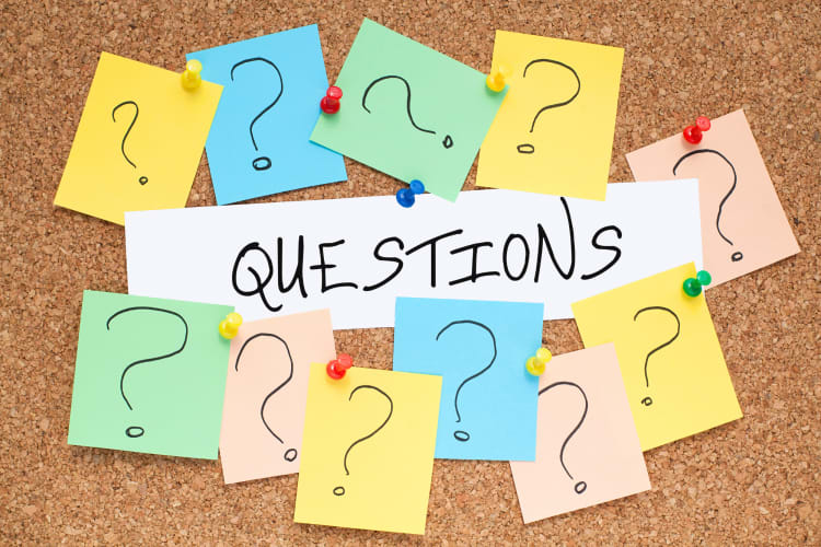 Questions marks on small pieces of notepad paper pinned to a board