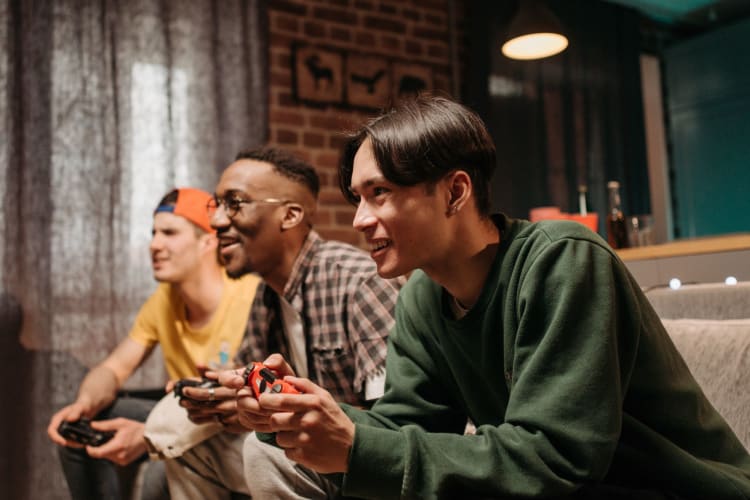 three men sit on a couch playing computer games and laughing