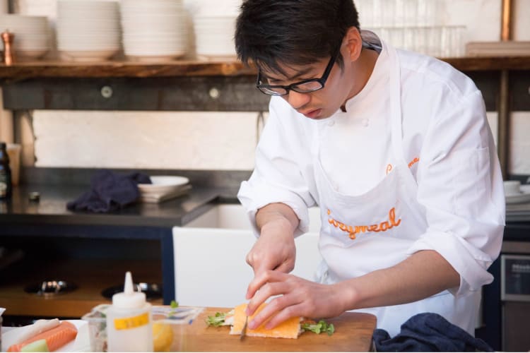 a chef in chef's whites carefully chops cheese with a sharp knife