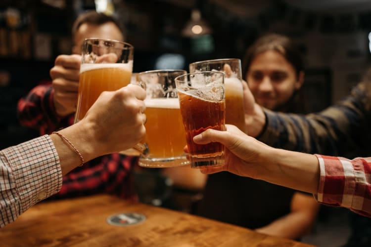 several hands hold up glasses of beer in a toast