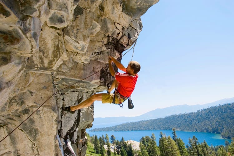 A person rock climbing next to evergreen forests and a lake