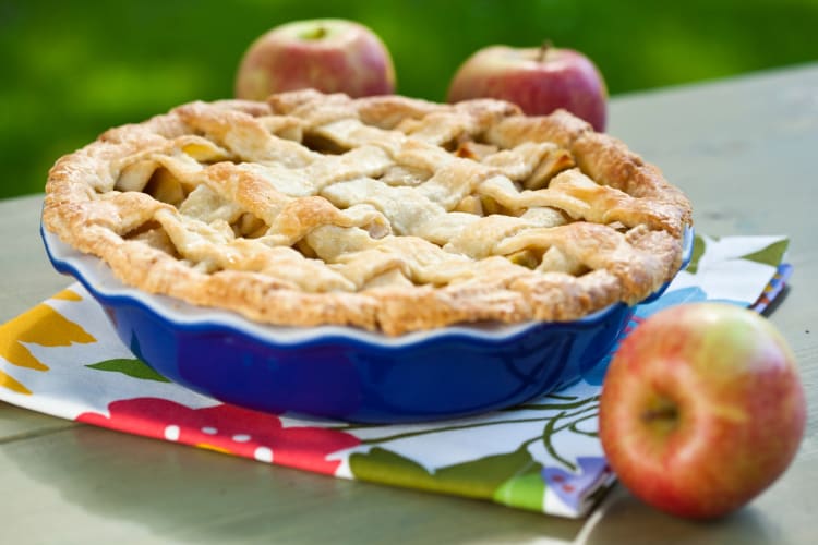 An apple pie next to fresh apples