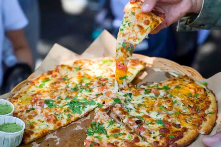 People taking slices of pizza from a whole pie