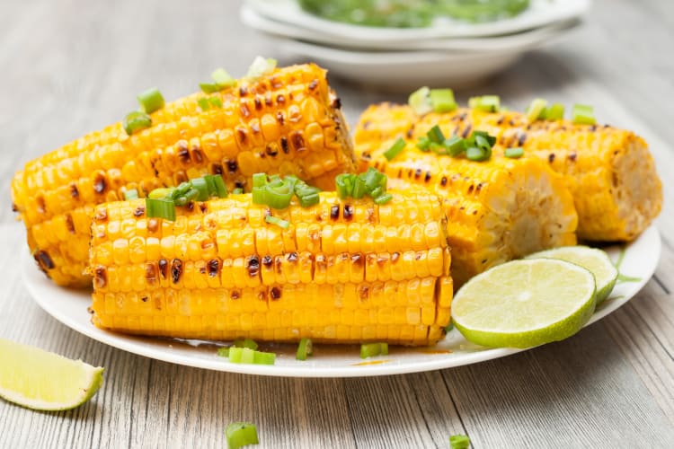 Corn on the cob on a plate next to limes