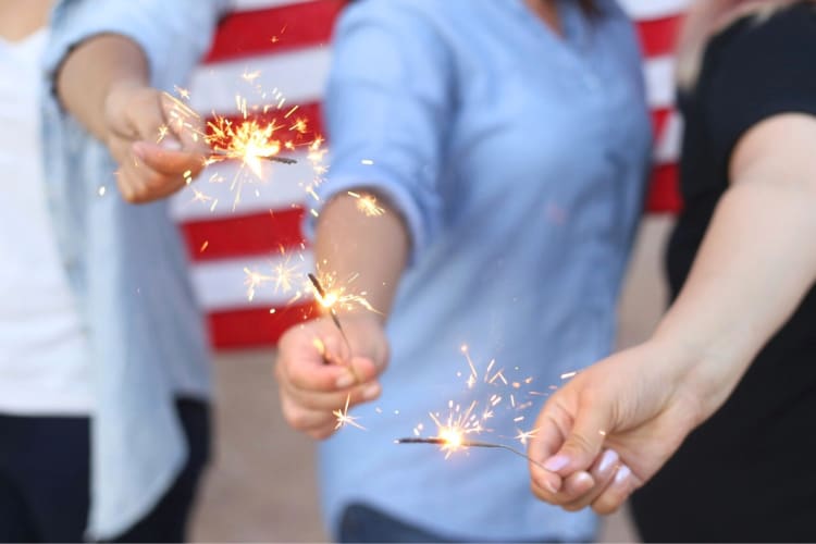 Three people holding sparklers in front of a US flag
