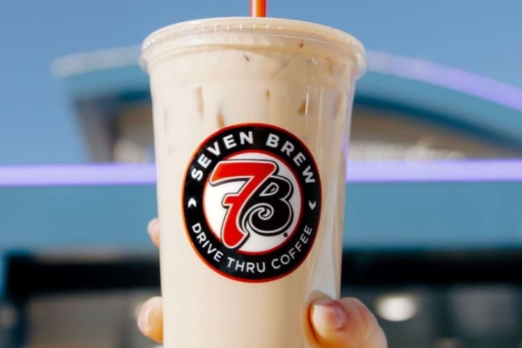 A cream colored coffee drink and a clear take out cup