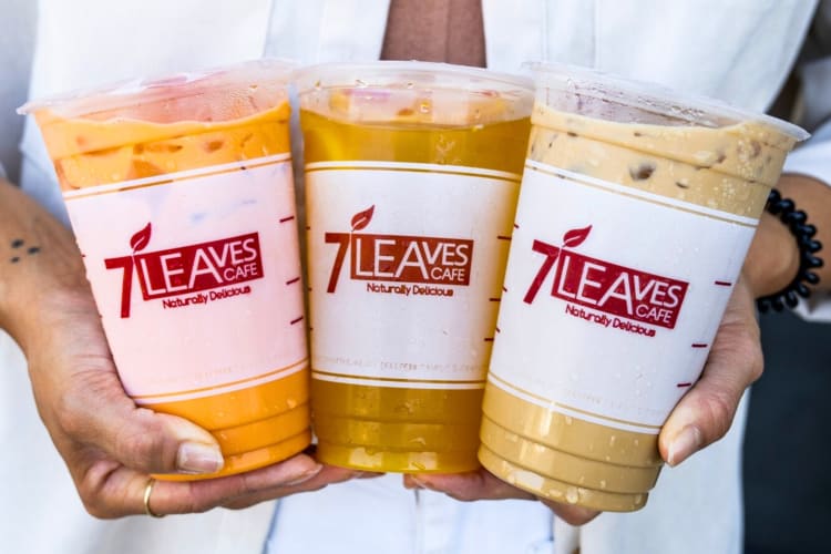 A person holding three take-out iced tea drinks in clear plastic cups