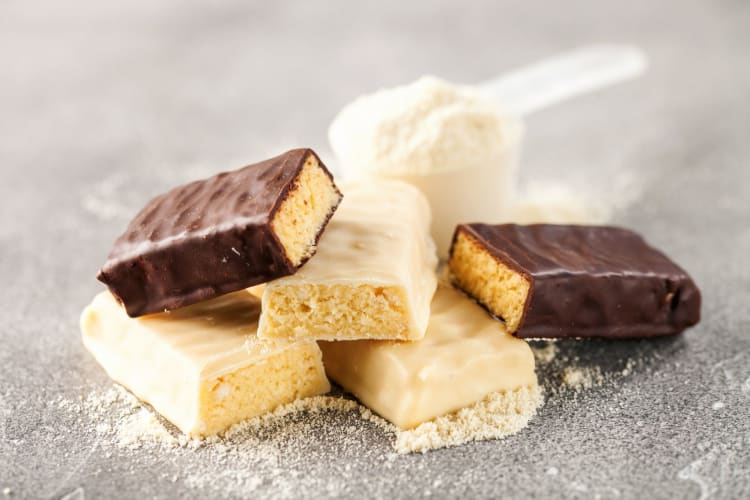 Whey protein powder in measuring scoop and different energy protein bars.