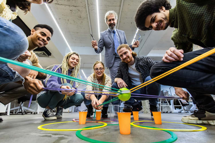 One person overseeing six others during a team building activity involving cups and a tennis ball