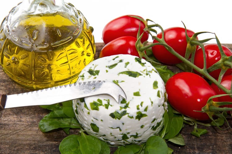 Goat cheese with tomatoes, leaves, a knife and olive oil