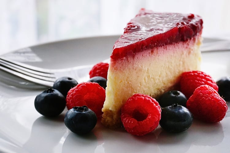 Closeup shot of a slice of cheesecake surrounded by blueberries and raspberries