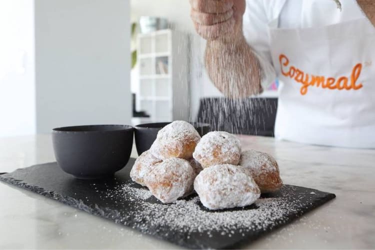 A chef putting powdered sugar onto beignets