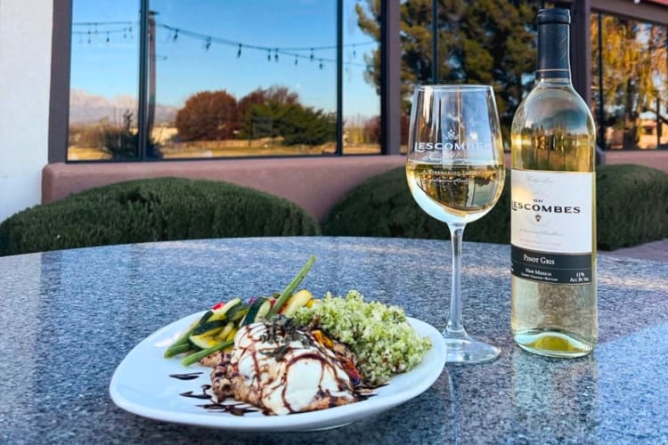 A glass and a bottle of wine next to a salad on a patio table